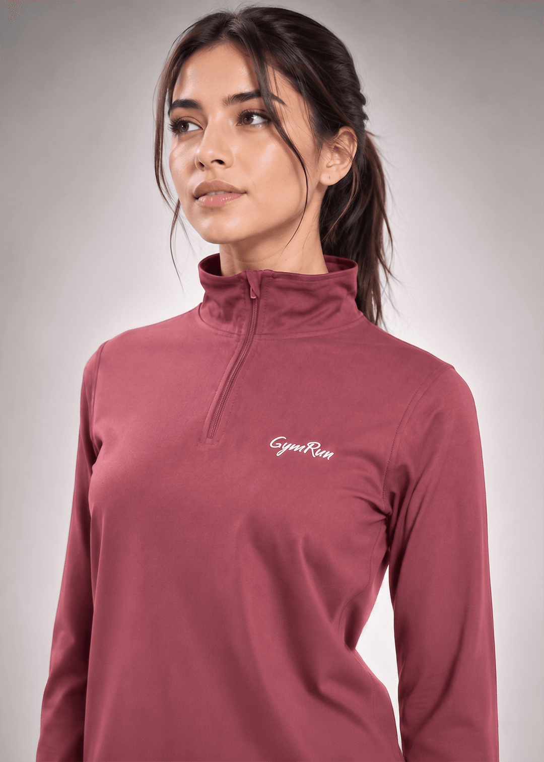 A woman wearing a muted rose-brown long-sleeve quarter-zip pullover with a white embroidered 'GymRun' logo on the left chest, set against a neutral gray studio background.