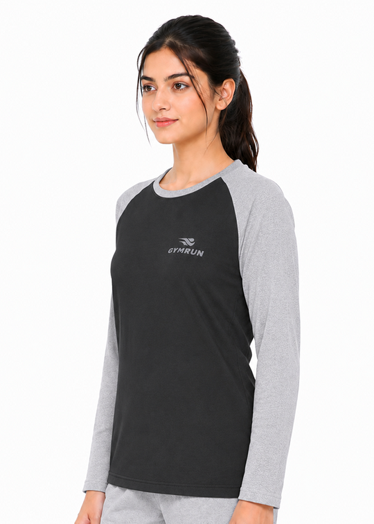 A woman modeling a long-sleeve raglan t-shirt in black and heather gray. The shirt features a black body, gray sleeves, and a small white GYMRUN logo on the left chest.