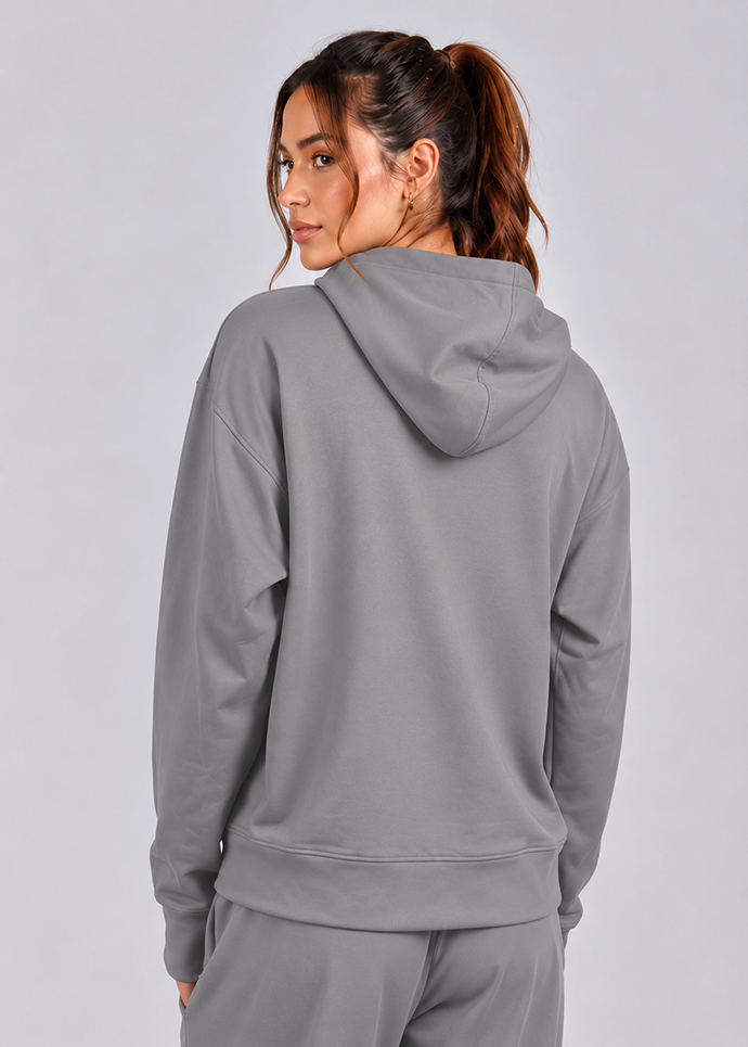 A woman shown from the back wearing a gray pullover hoodie and matching gray sweatpants against a light gray studio background.