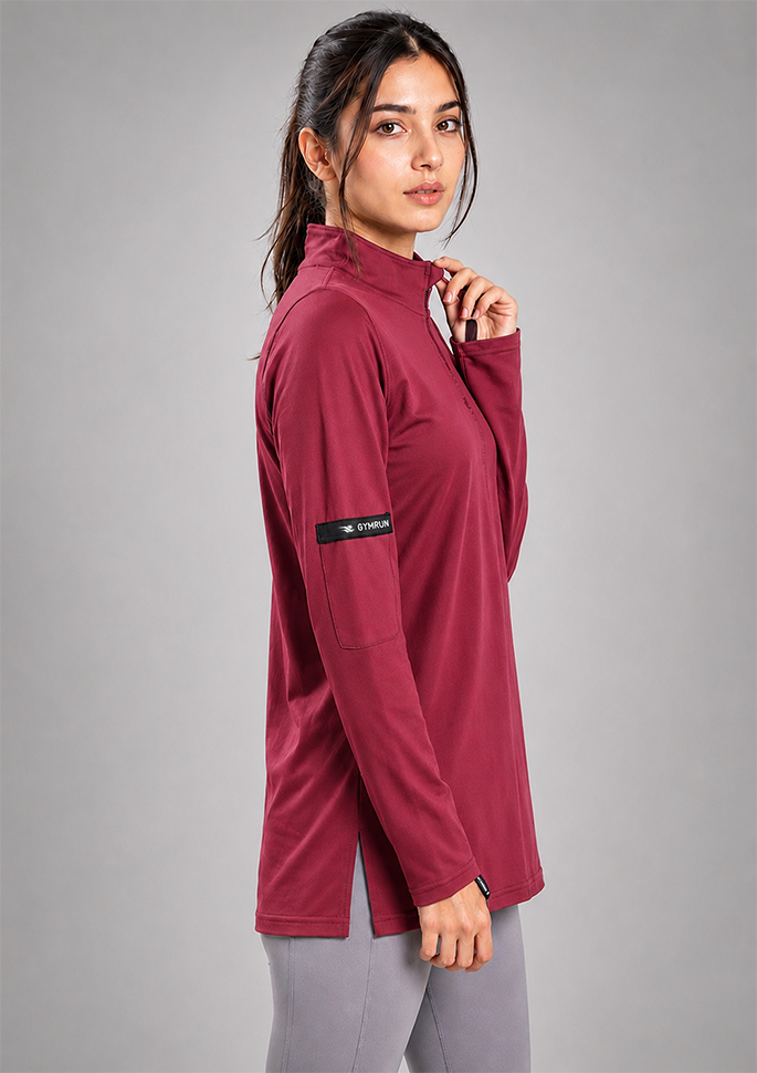 A woman modeling a long-sleeve athletic quarter-zip top in deep burgundy, paired with gray leggings, against a solid gray studio background.