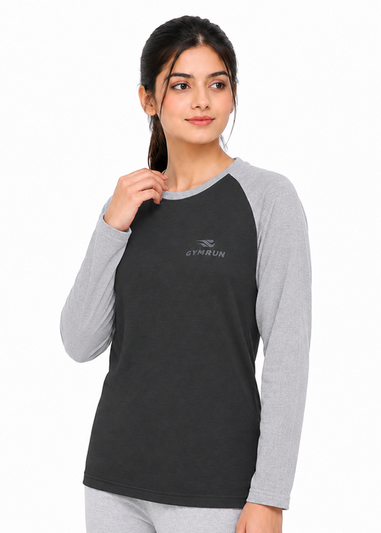 A woman modeling a dark charcoal gray long-sleeve raglan t-shirt with light gray sleeves and collar, featuring a small gray GYMRUN logo on the chest, set against a plain white background.