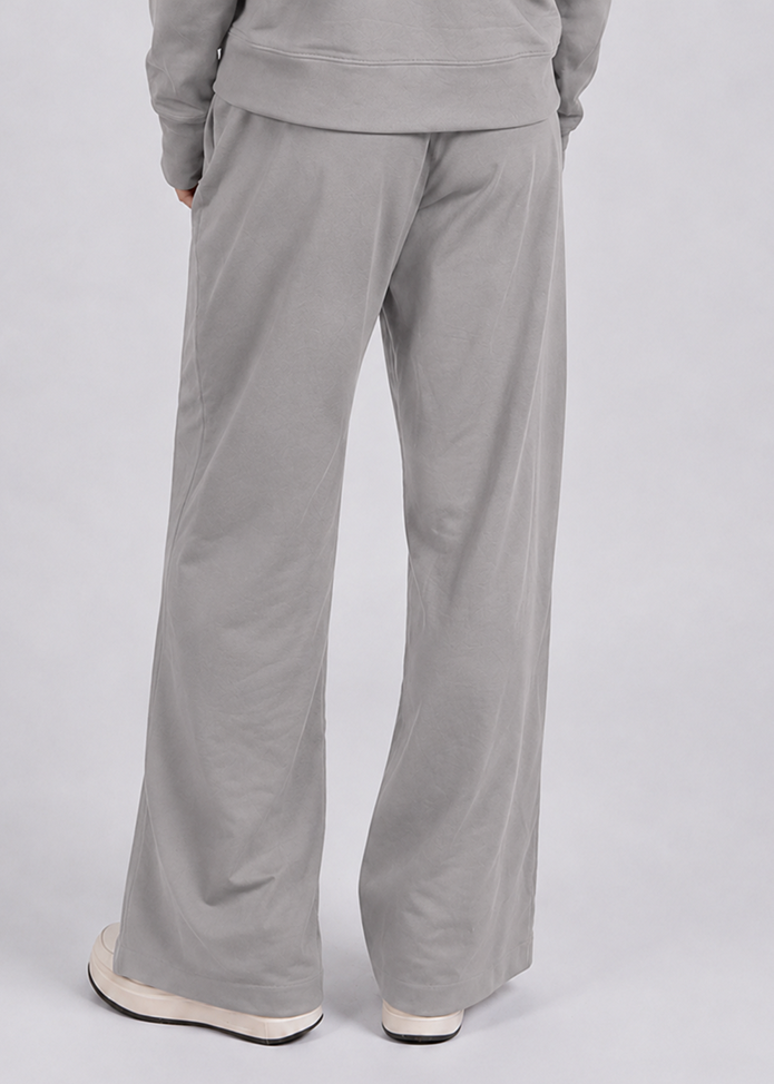 A person shown from the back wearing light gray wide-leg sweatpants and a matching gray sweatshirt, paired with white sneakers, against a plain light gray studio background.