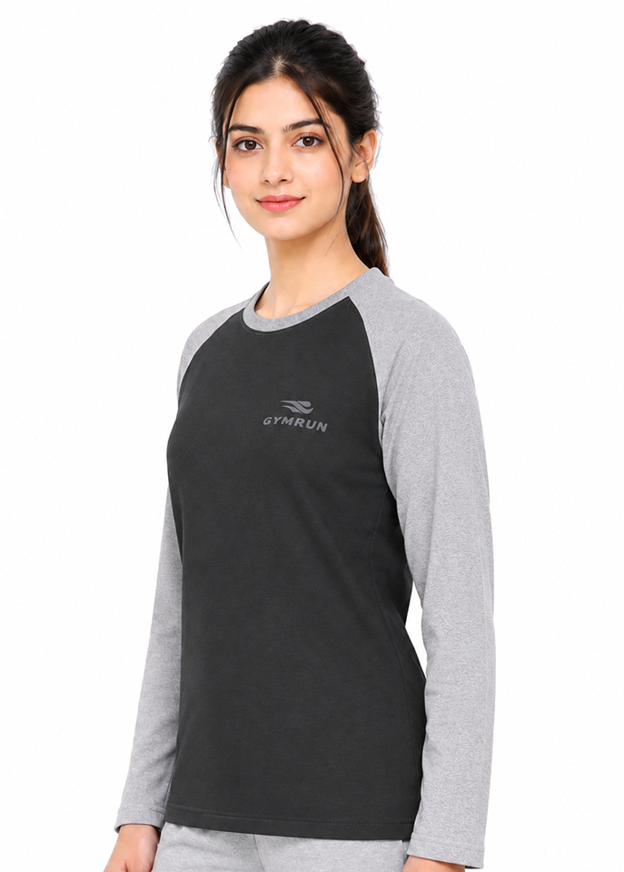 A woman modeling a long-sleeve athletic shirt with a black body and heather gray raglan sleeves, featuring a small gray GYMRUN logo on the left chest, against a plain white background.